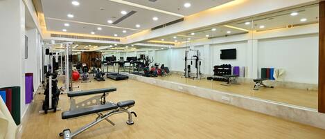 Un gimnasio amplio con diversos equipos de ejercicio, un gran ventanal de espejos y suelo de madera.