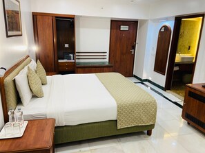 Habitación de hotel con cama, mesita de noche, armario y un baño visible a través de una puerta abierta.