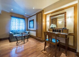 A room with a wooden desk, a chair, a sofa, and a small table with flowers.