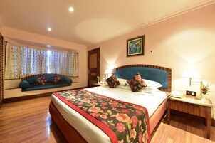 A hotel room with a large bed, a sofa bed, a bedside table with a lamp, and a window with curtains.
