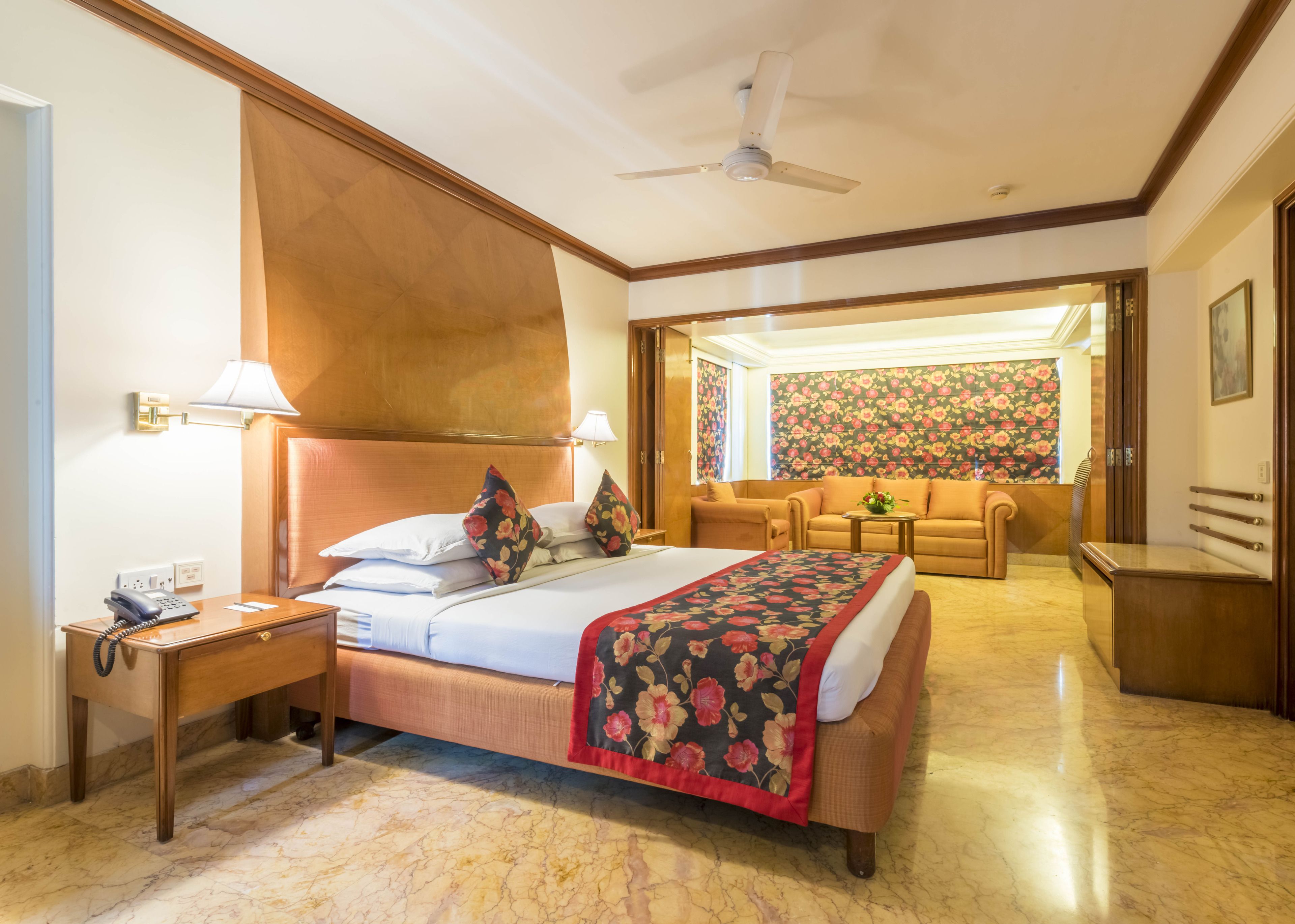 A hotel room with a bed, a desk with a telephone, a chair, a sofa, and a ceiling fan.