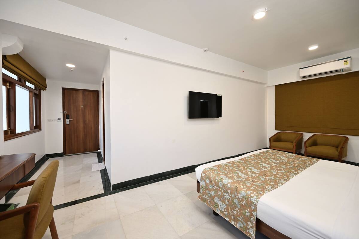 Quarto de hotel com cama, escrivaninha, cadeira, televisão e ar condicionado.