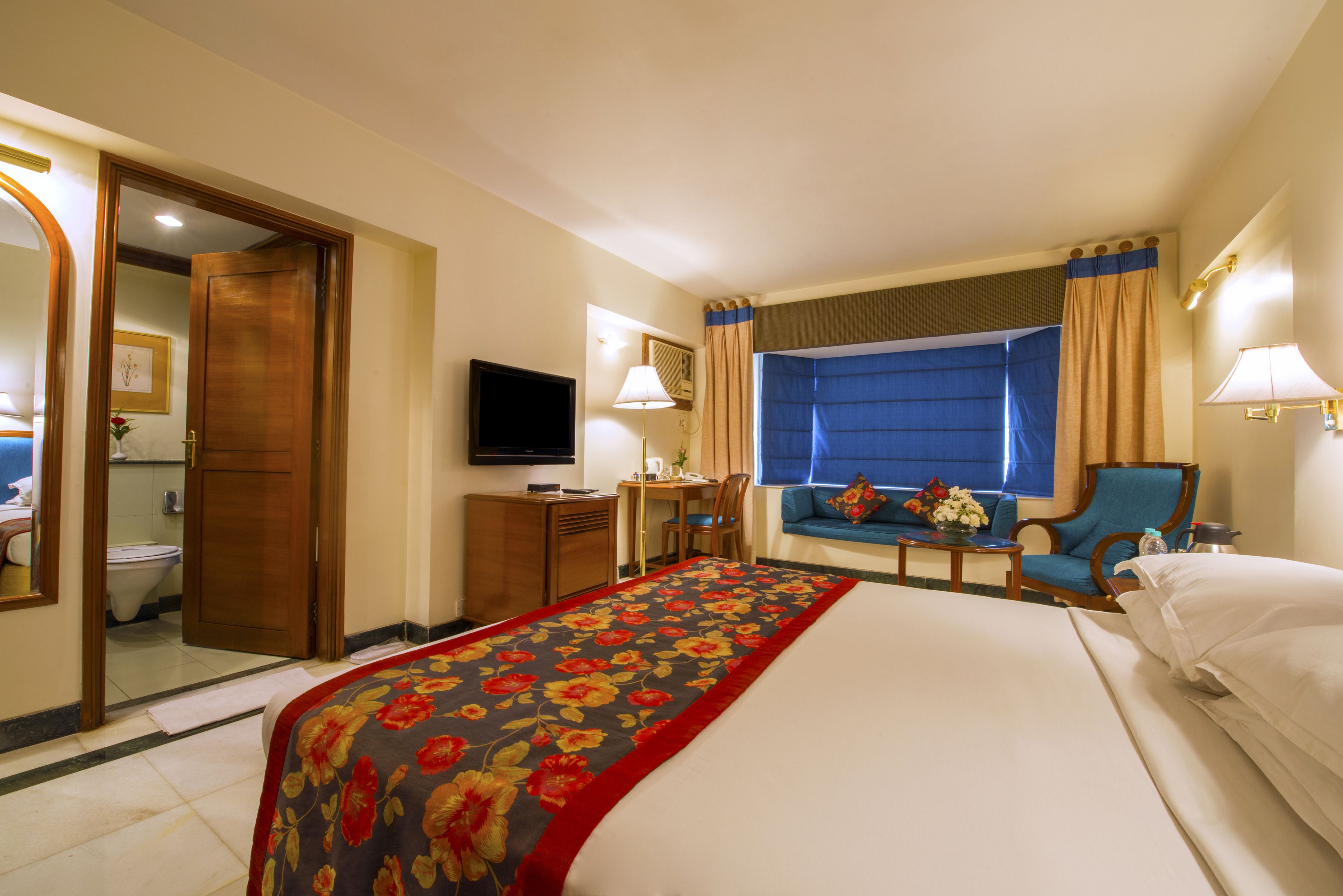 A hotel room with a large bed, a desk with a chair, a television, and a window with curtains.