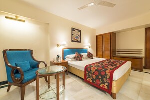 Een hotelkamer met een bed, een stoel, een klein tafeltje en een nachtkastje.