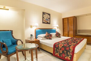 A hotel room with a bed, a blue armchair, a small table, and a wooden wardrobe.