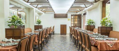 A dining area with long tables, chairs, and potted plants.