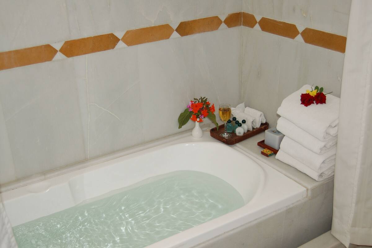 Une baignoire agrémentée d’un arrangement floral, un verre contenant un liquide et des serviettes soigneusement pliées.