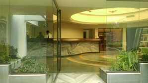 A lobby with a reception desk, a curved seating area, and potted plants. - The Meadows Resort and Spa (Chhatrapati Sambhajinagar)