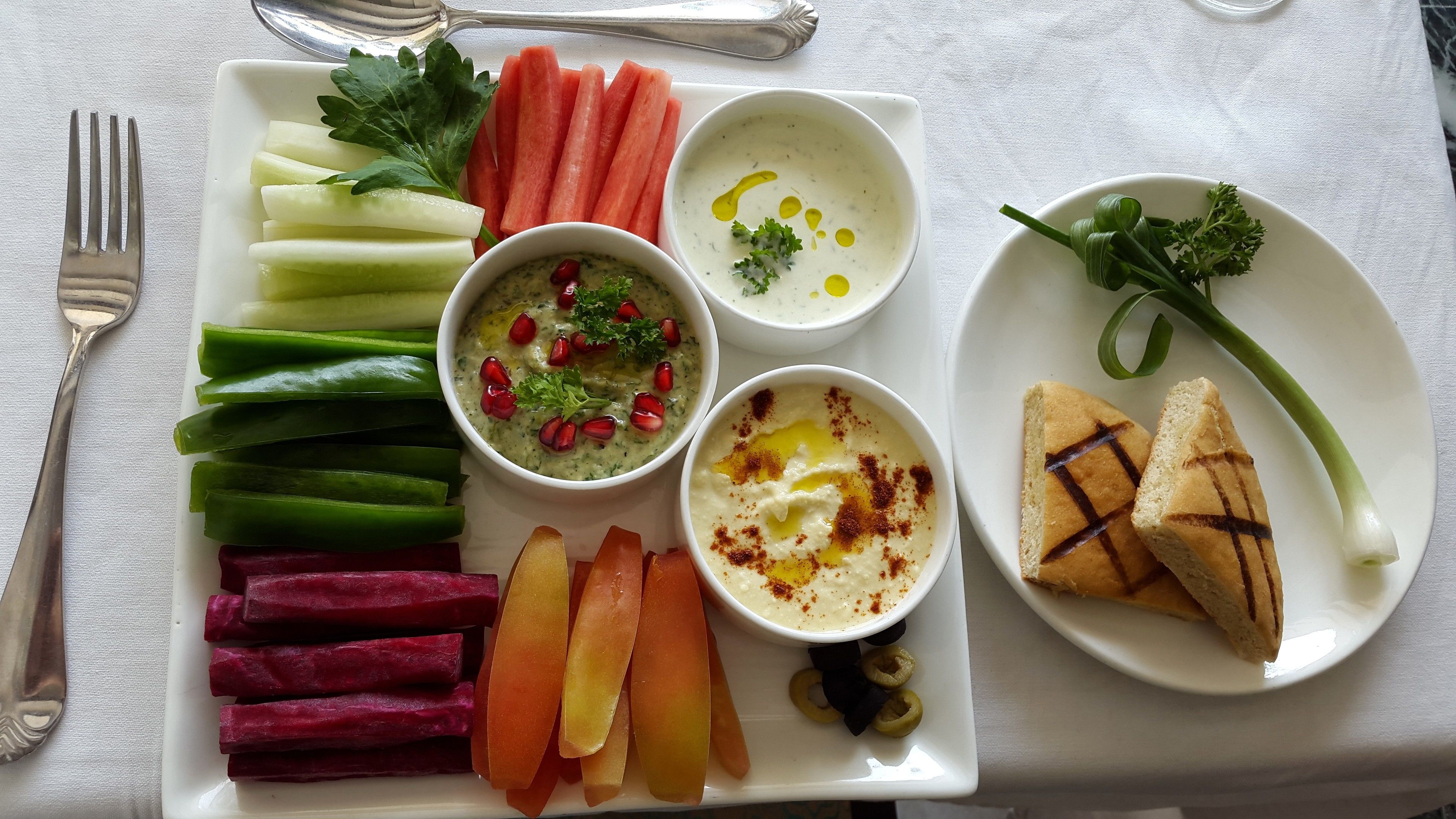 A plate with various food items including vegetables, dips, and bread.