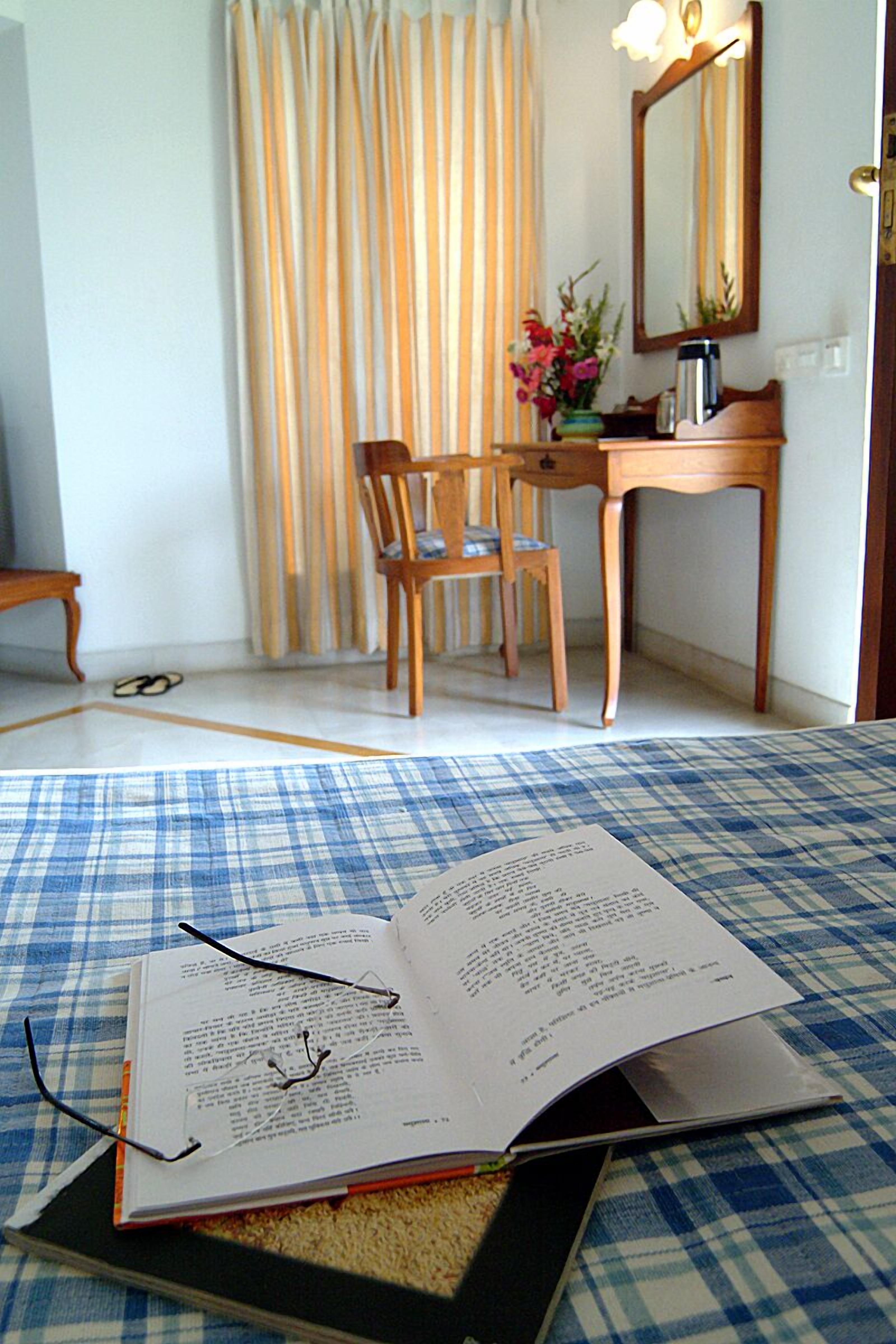 Una habitación con piso a cuadros, un escritorio con espejo, una silla y un jarrón con flores.