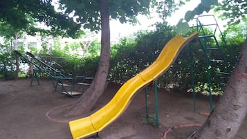 Children can play and climb in the shaded playground area surrounded by trees.