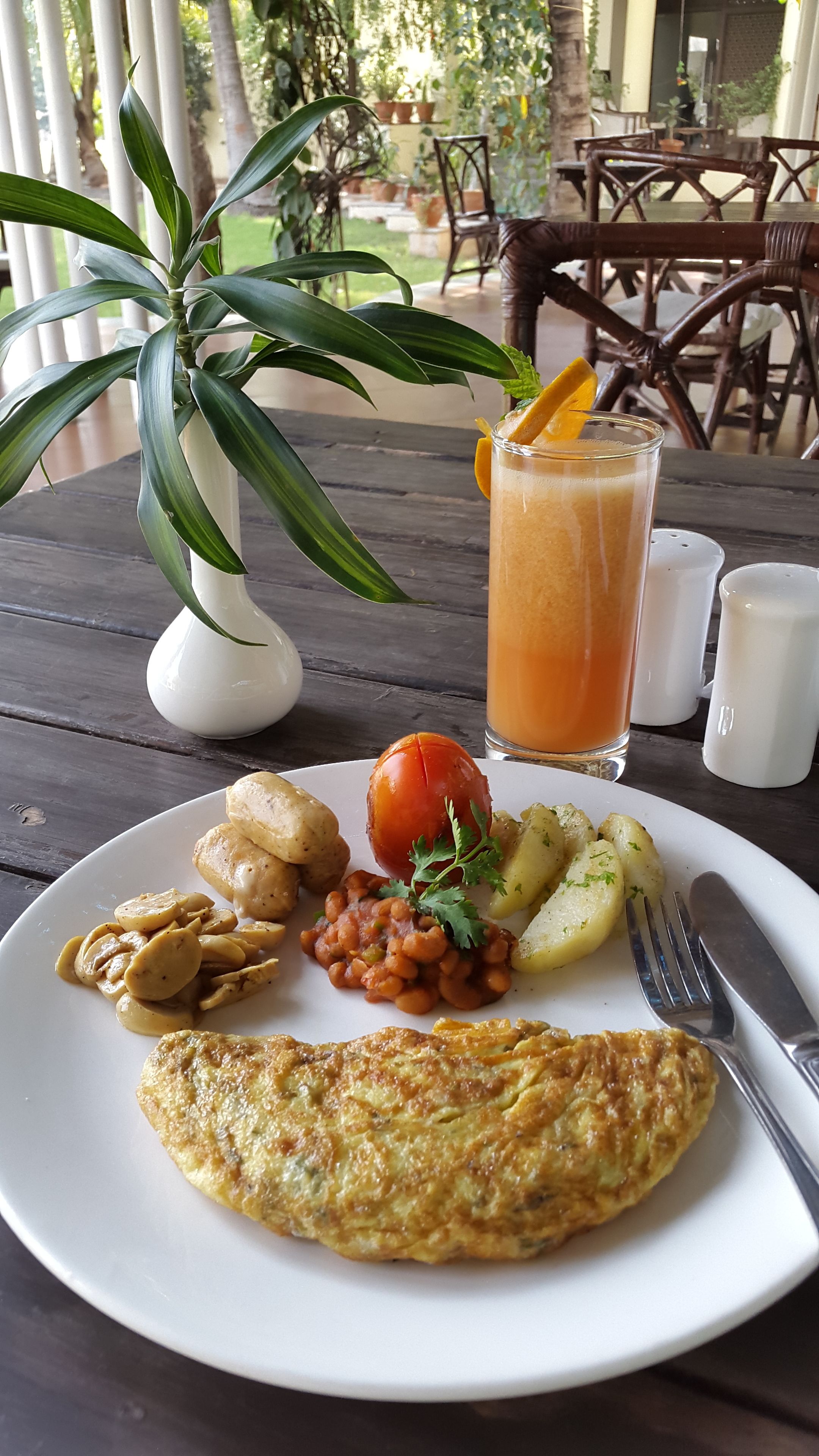 Une assiette de nourriture contenant une omelette, des pommes de terre, des haricots et une tomate, le tout posé sur une table en bois.