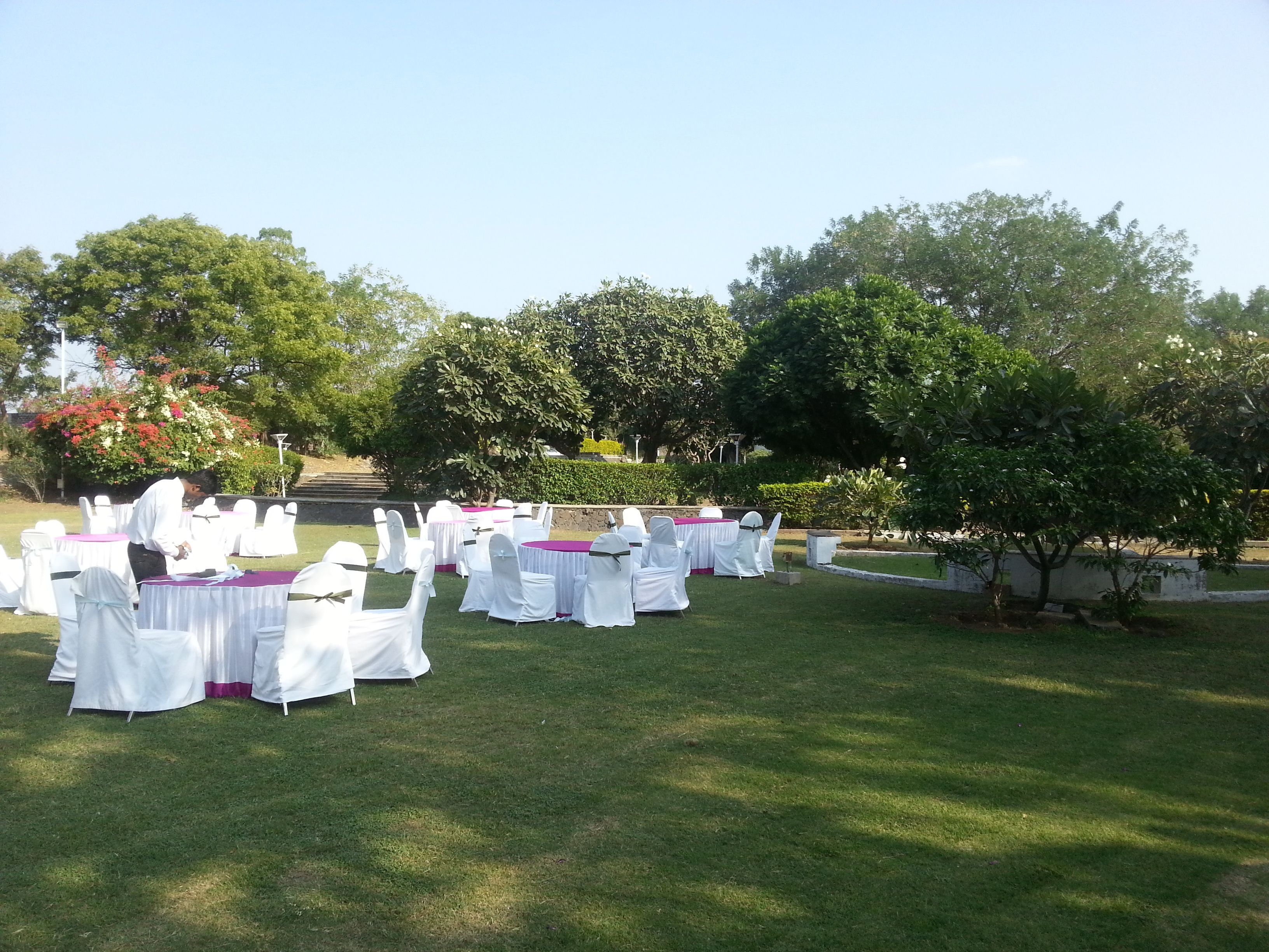 An outdoor event setup with round tables covered in white tablecloths and chairs with white covers.