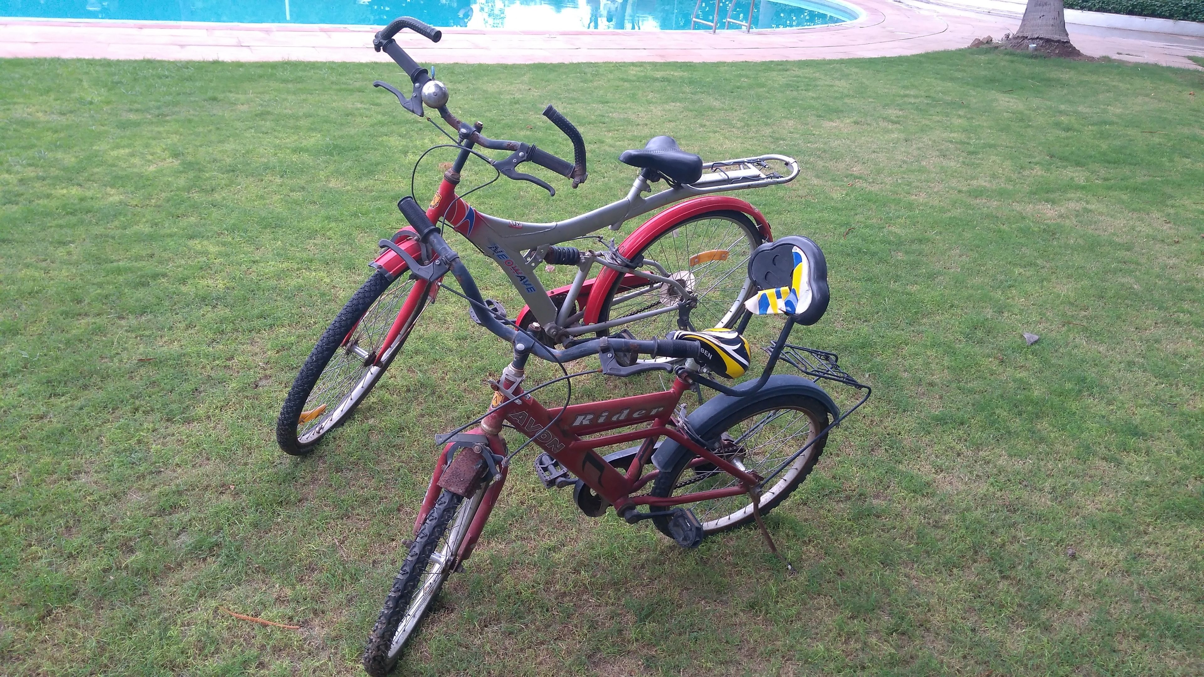 A red bicycle with a front basket and a rear rack, parked on a grassy lawn.