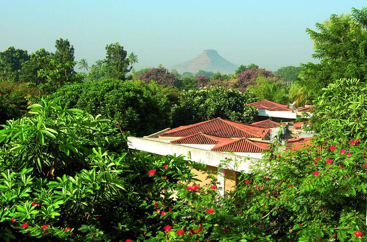 A building with a red-tiled roof surrounded by lush greenery and red flowers.