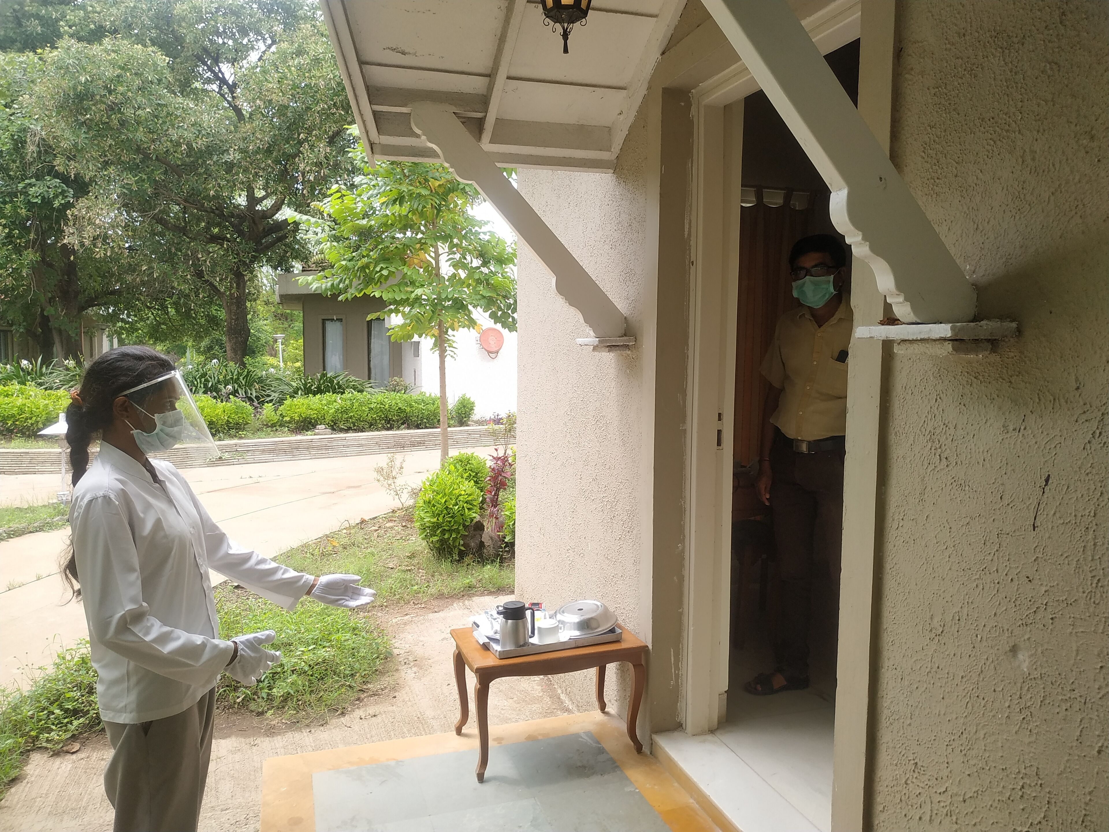 A person standing at the entrance of a building, gesturing towards the door.