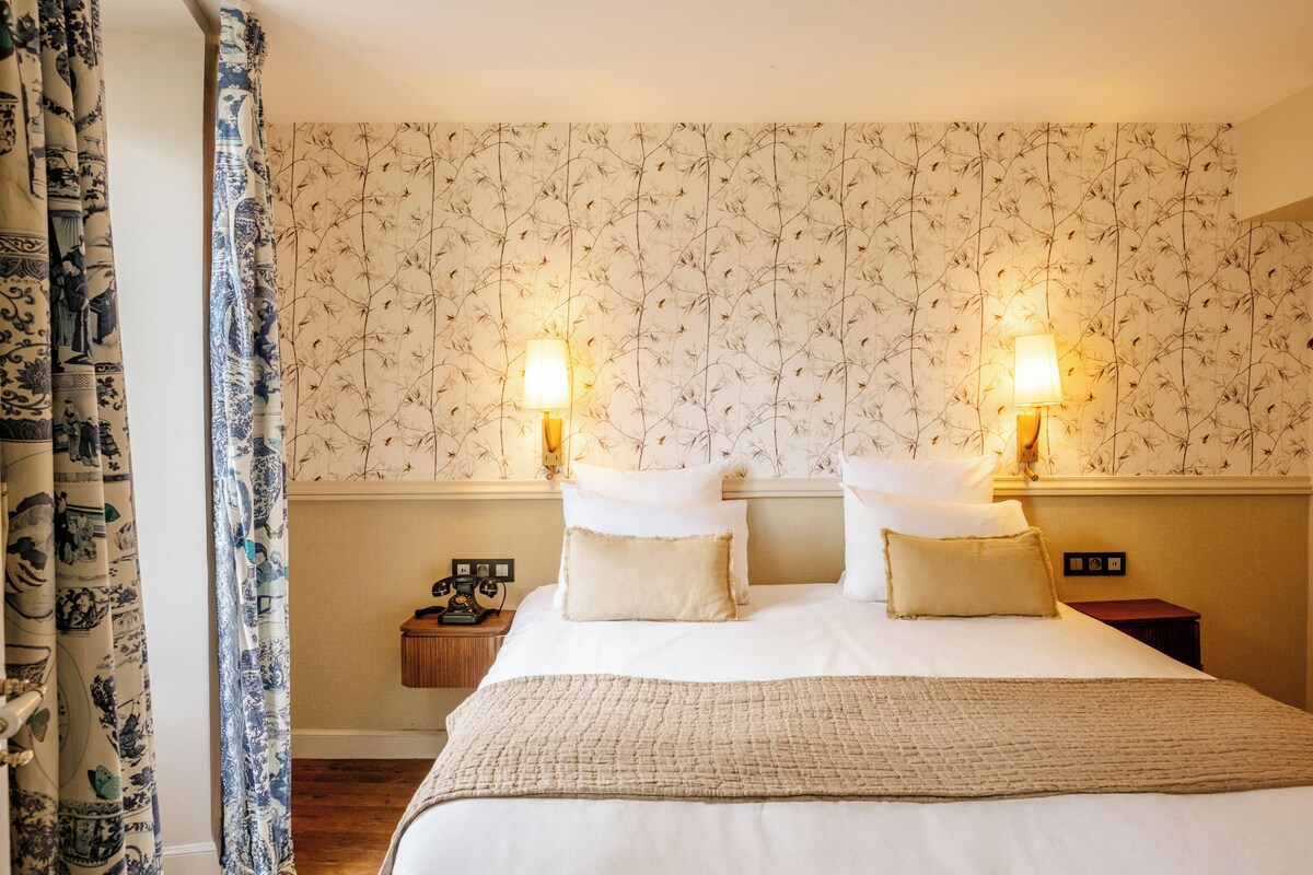 A hotel room with a large bed, two bedside lamps, a nightstand, and a patterned wallpaper.