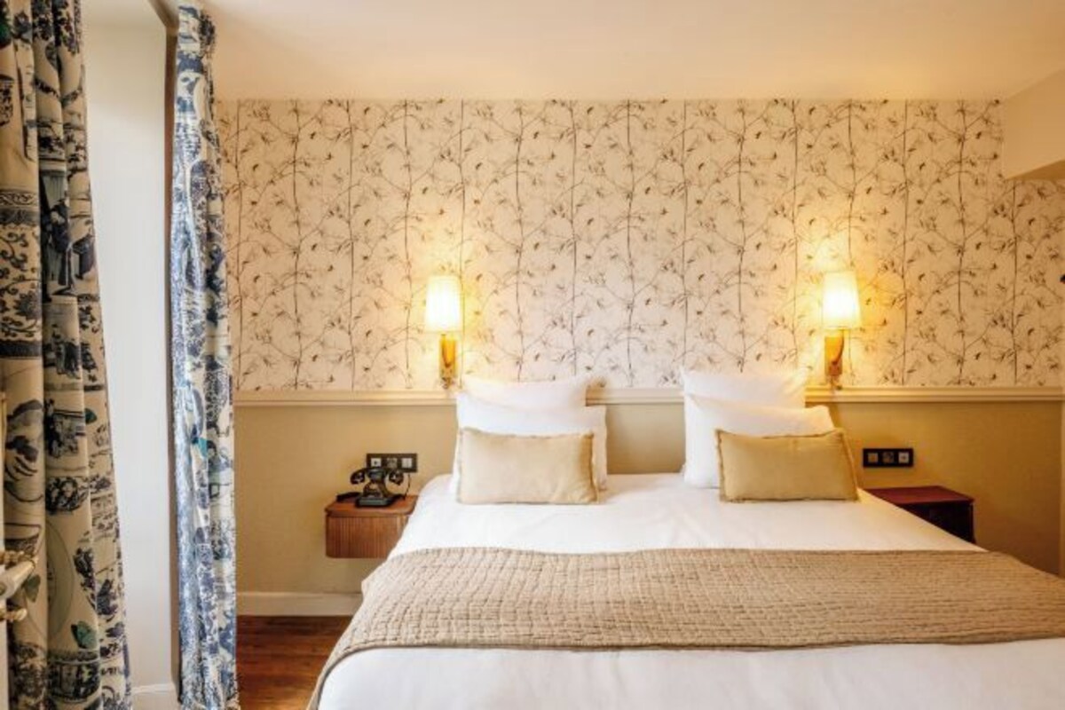 A hotel room with a bed, two bedside lamps, a nightstand, and a patterned wallpaper.