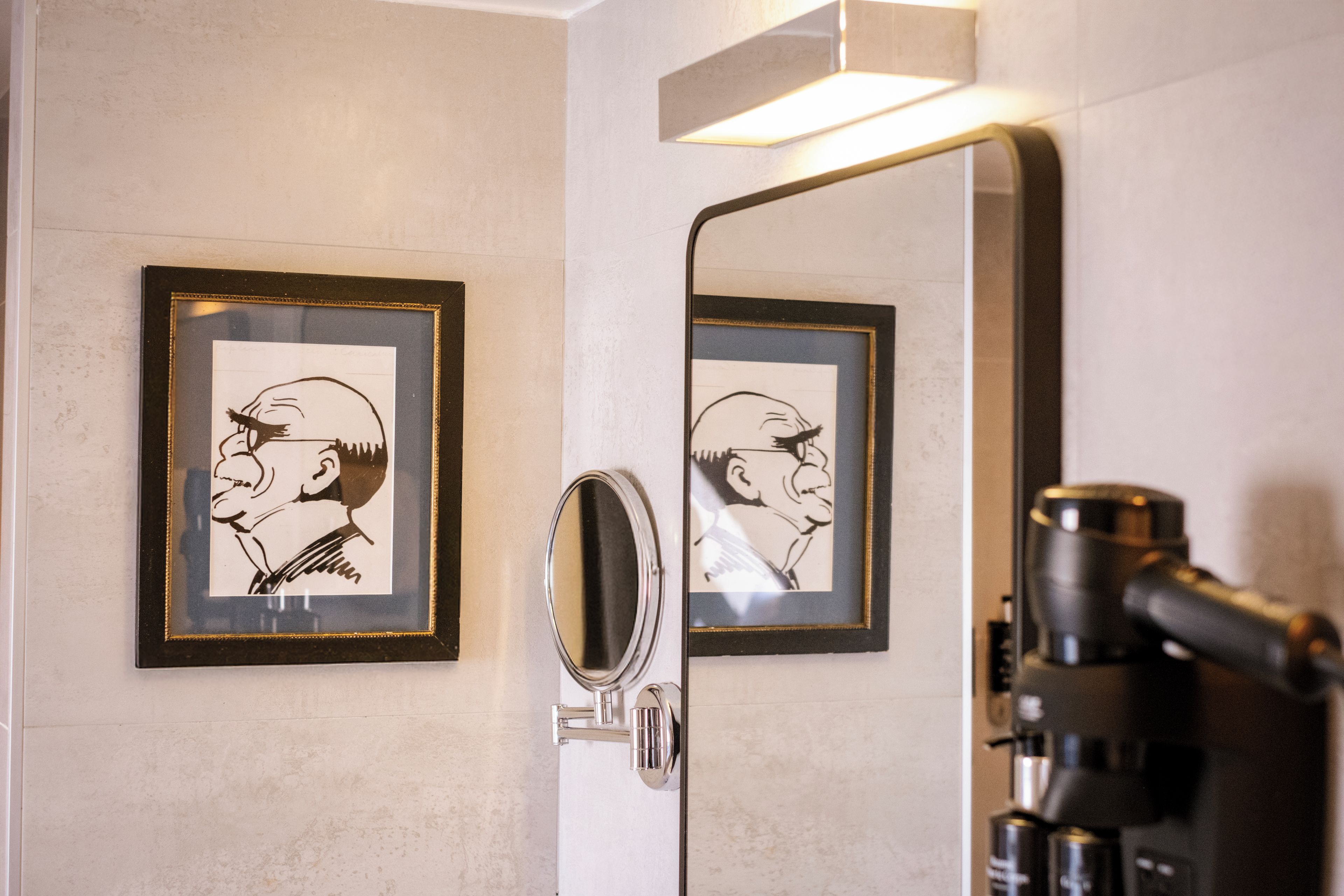 Une salle de bain avec un miroir, deux portraits en noir et blanc encadrés et une machine à café.