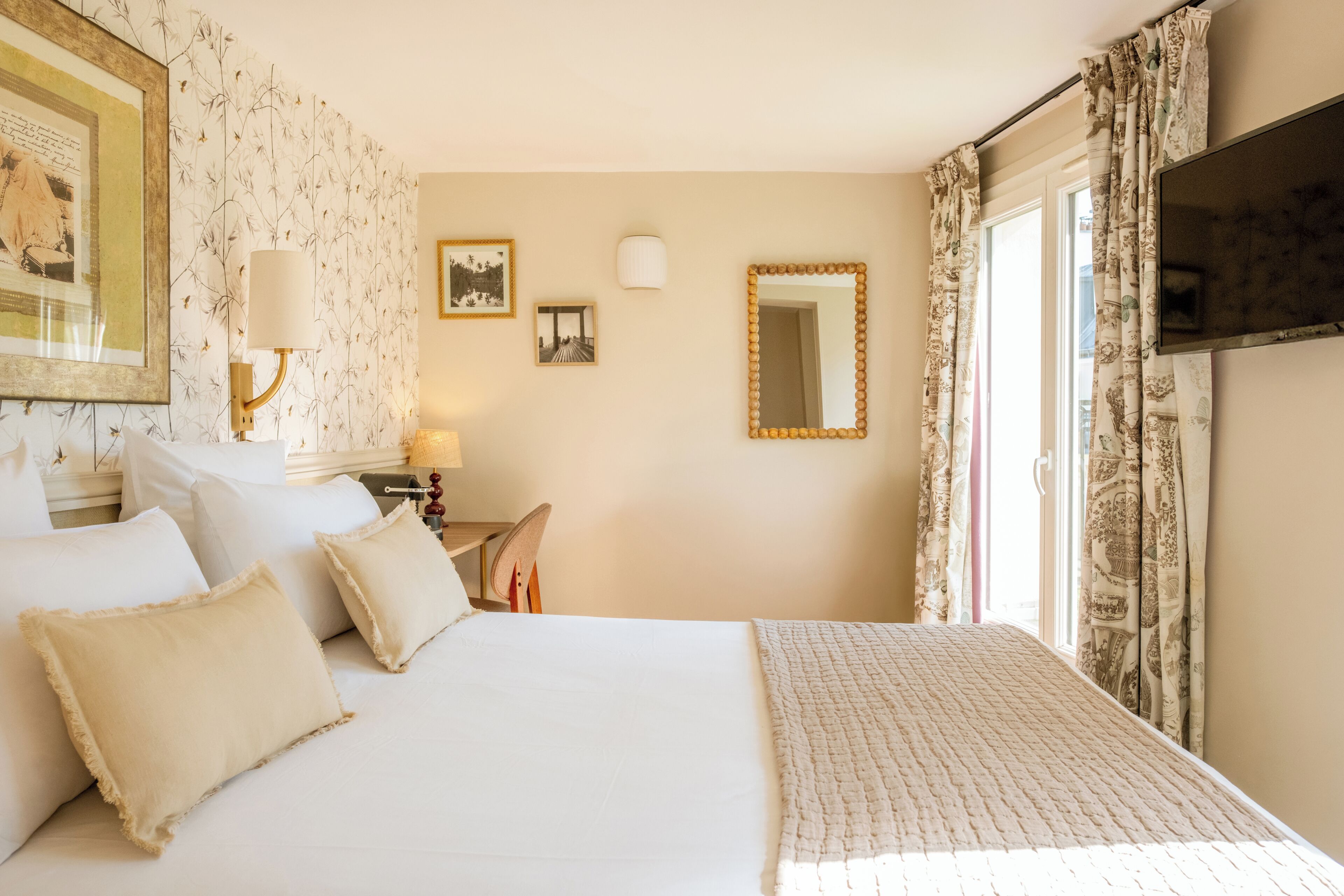 A hotel room with a bed, pillows, a desk with a lamp, a mirror, and a television.