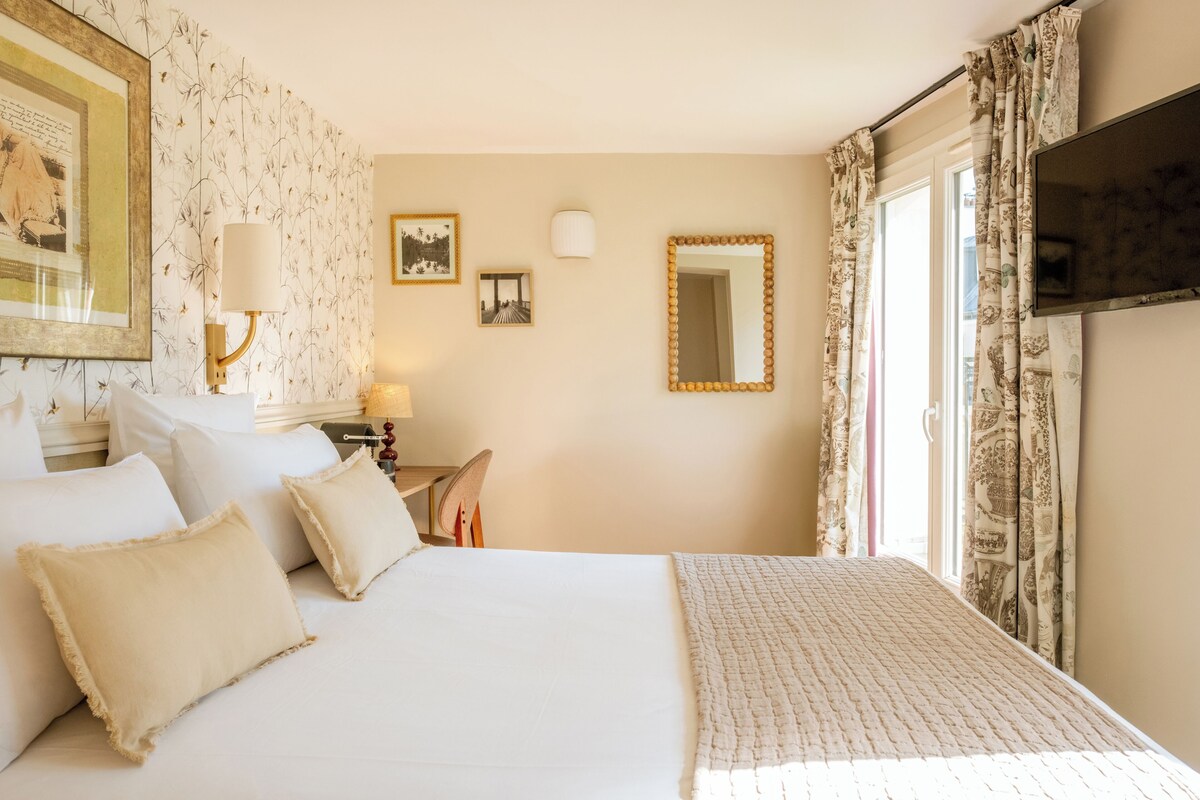A hotel room with a bed, pillows, a desk with a lamp, a mirror, and a television.