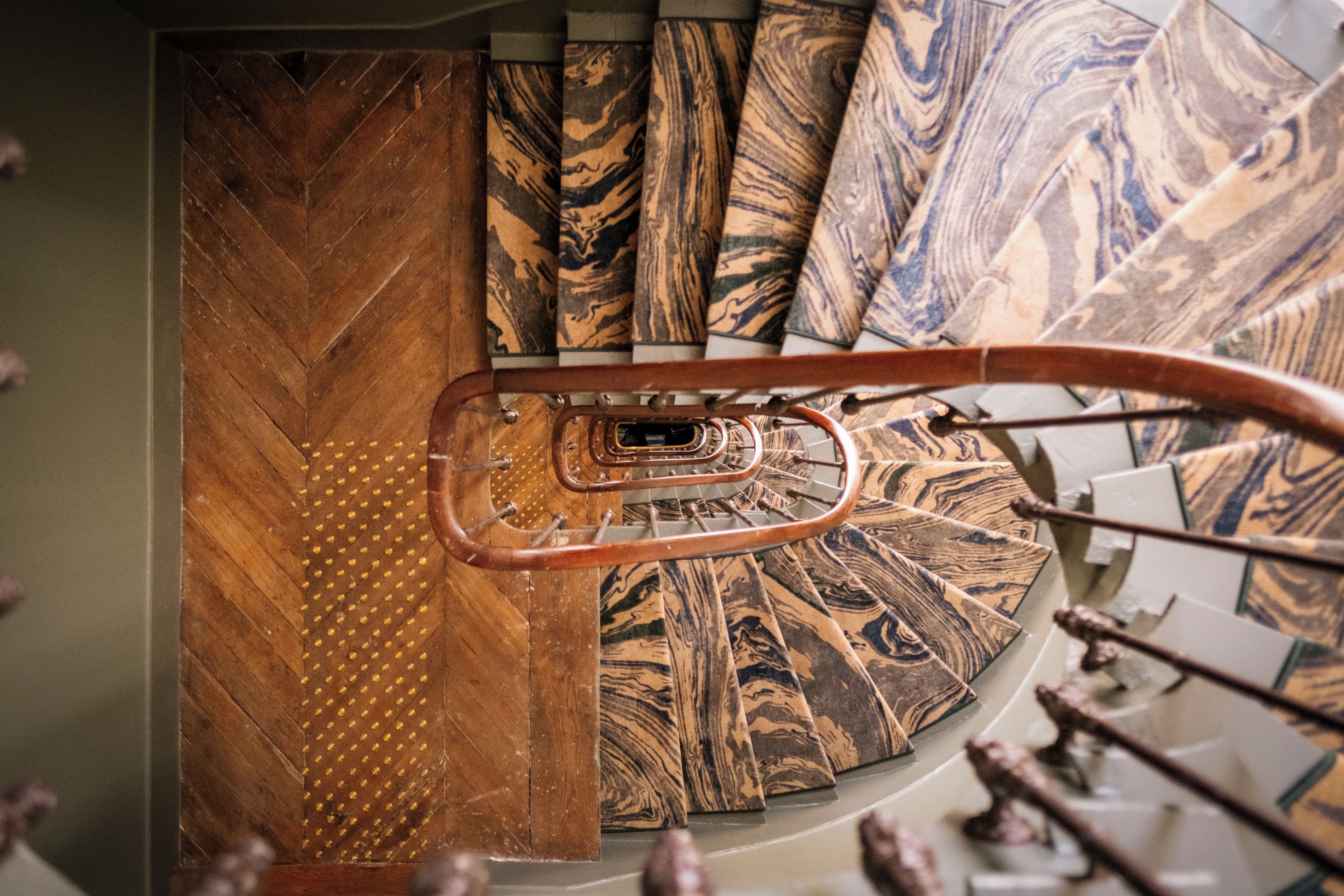 A spiral staircase with a wooden handrail and patterned carpet.