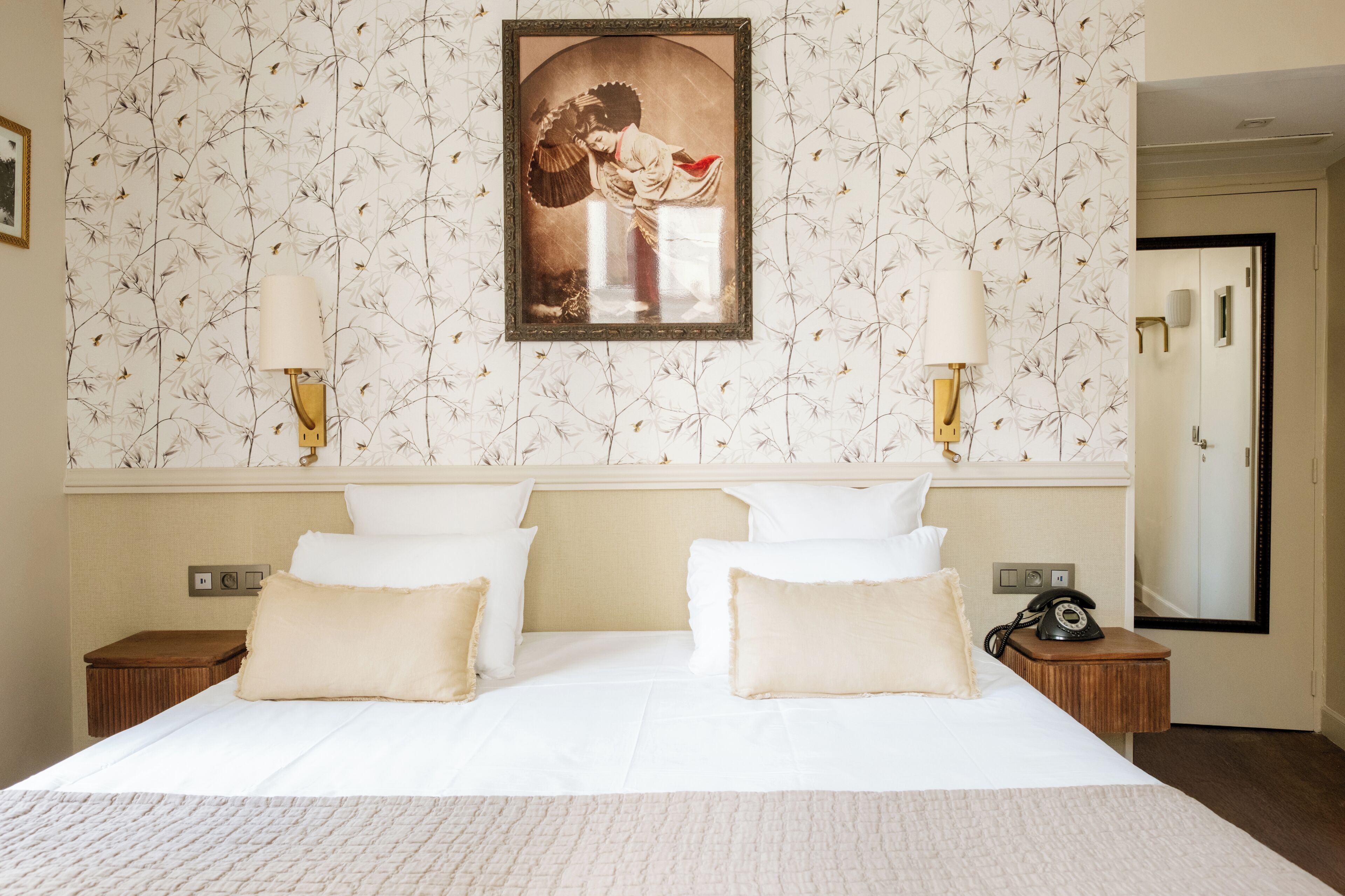 Una habitación de hotel con una cama grande, dos mesitas de noche, un cuadro en la pared y una puerta al fondo.