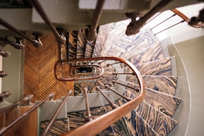 Un escalier en colimaçon dont les marches présentent un motif évoquant le marbre et qui est doté d’une rampe en métal.