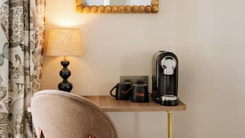 Habitación de hotel con escritorio, lámpara, dos tazas, cafetera y una silla.