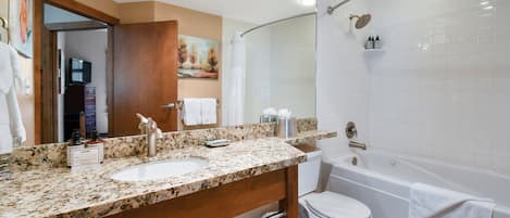 Un baño con lavamanos de encimera de granito, espejo, inodoro y bañera.