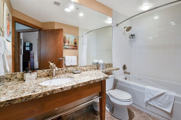 A bathroom with a granite countertop sink, a mirror, a toilet, and a bathtub.
