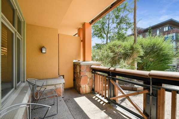 A balcony with a stone wall, a small table, and metal chairs.