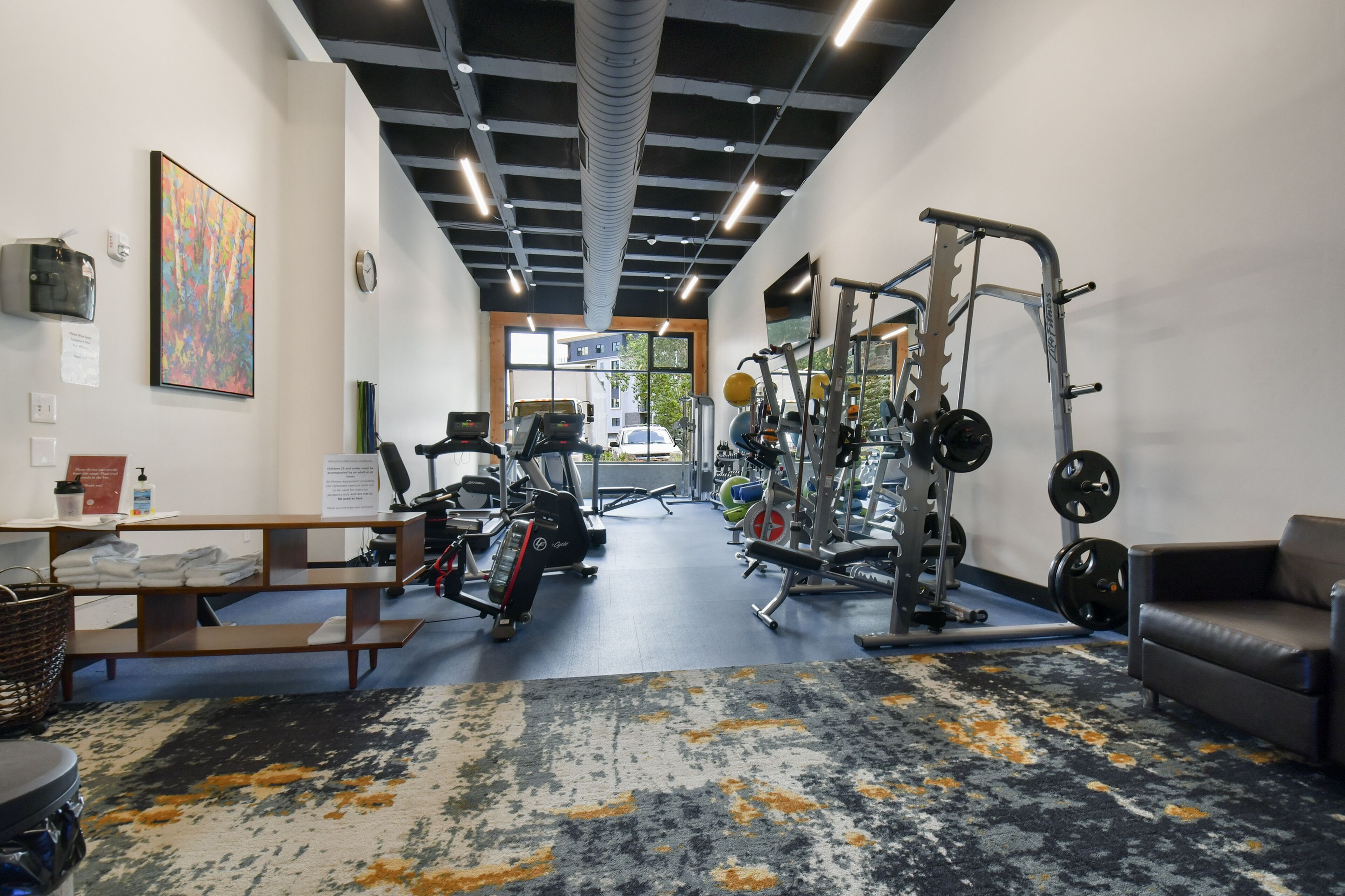 Un gimnasio con equipo de ejercicio, una recepción y un ventanal grande.