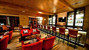 A bar area with red upholstered chairs, a wooden ceiling, and a bar counter with a television above it.