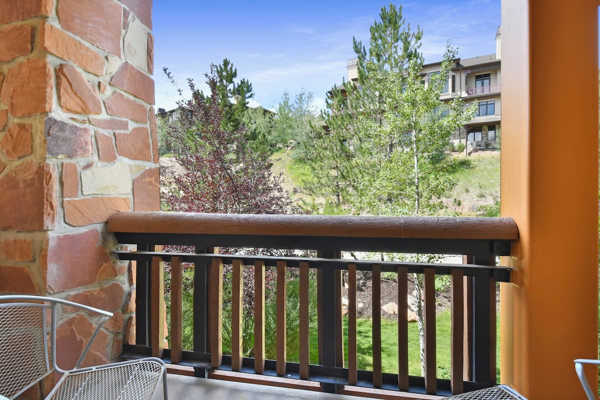 A balcony with a stone wall, wooden railing, and metal chairs.