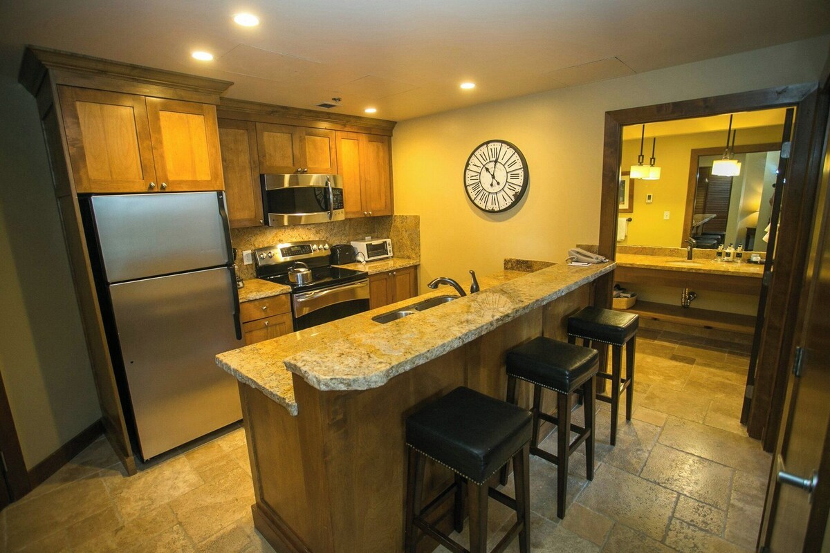 A kitchen with wooden cabinets, stainless steel appliances, granite countertops, and a large wall clock.