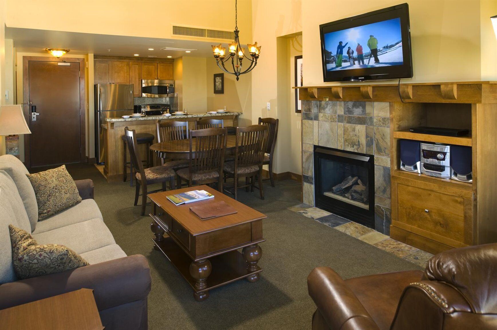 A living room with a fireplace, a television, and a kitchen in the background.
