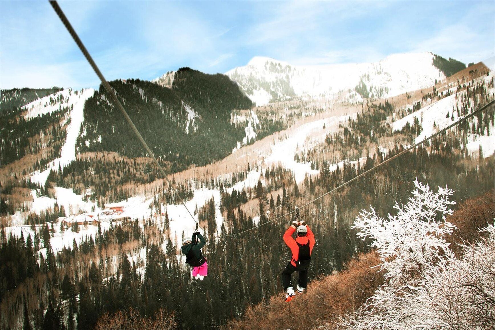 A mountainous landscape with a ski lift and a person in a red jacket standing on a snowy slope.