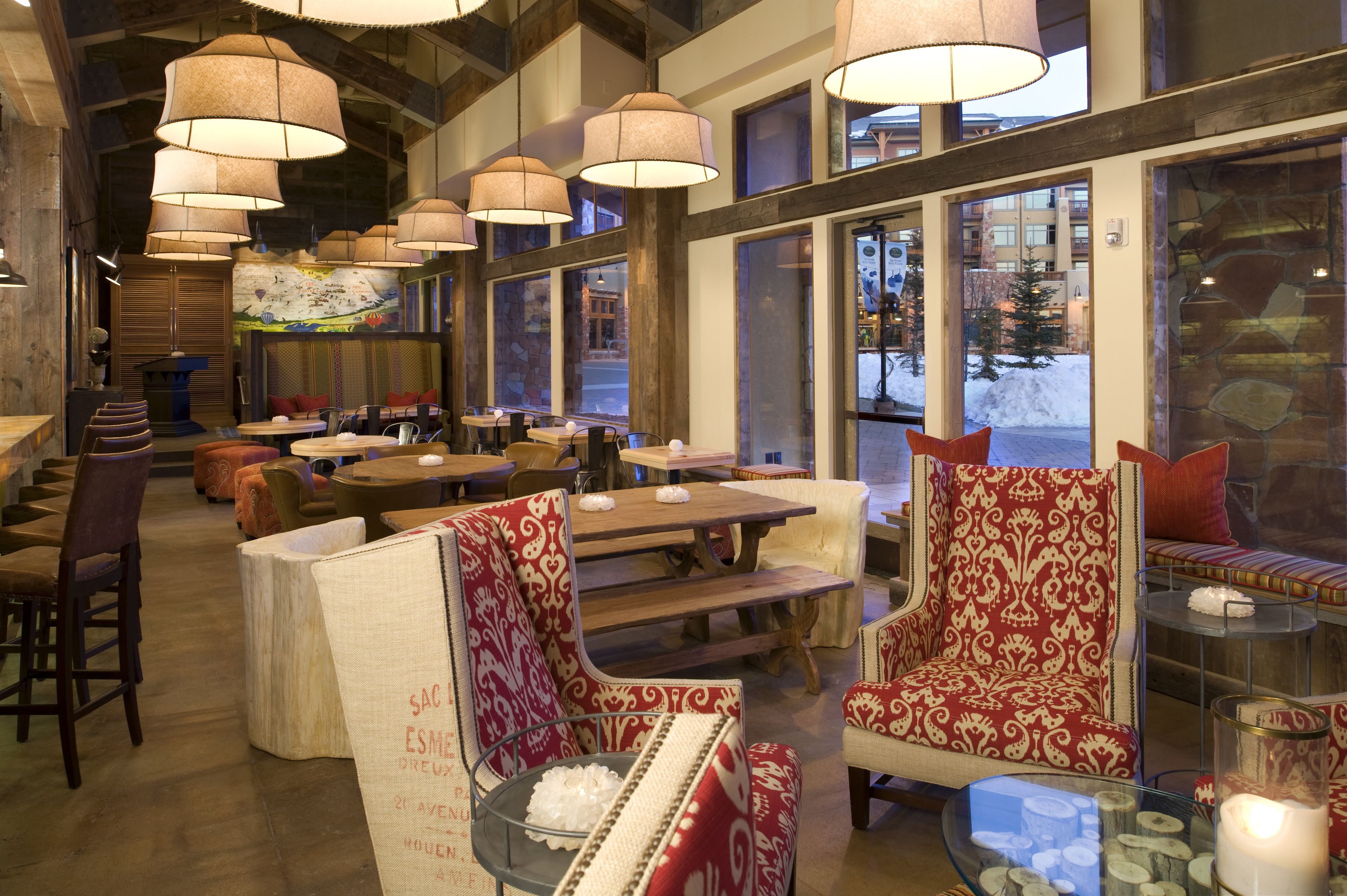 A cozy restaurant interior with wooden tables and chairs, large windows, and hanging lamps.