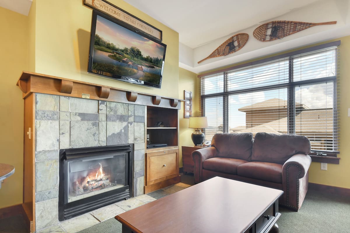 A living room with a fireplace, a leather sofa, and a television mounted above the fireplace.