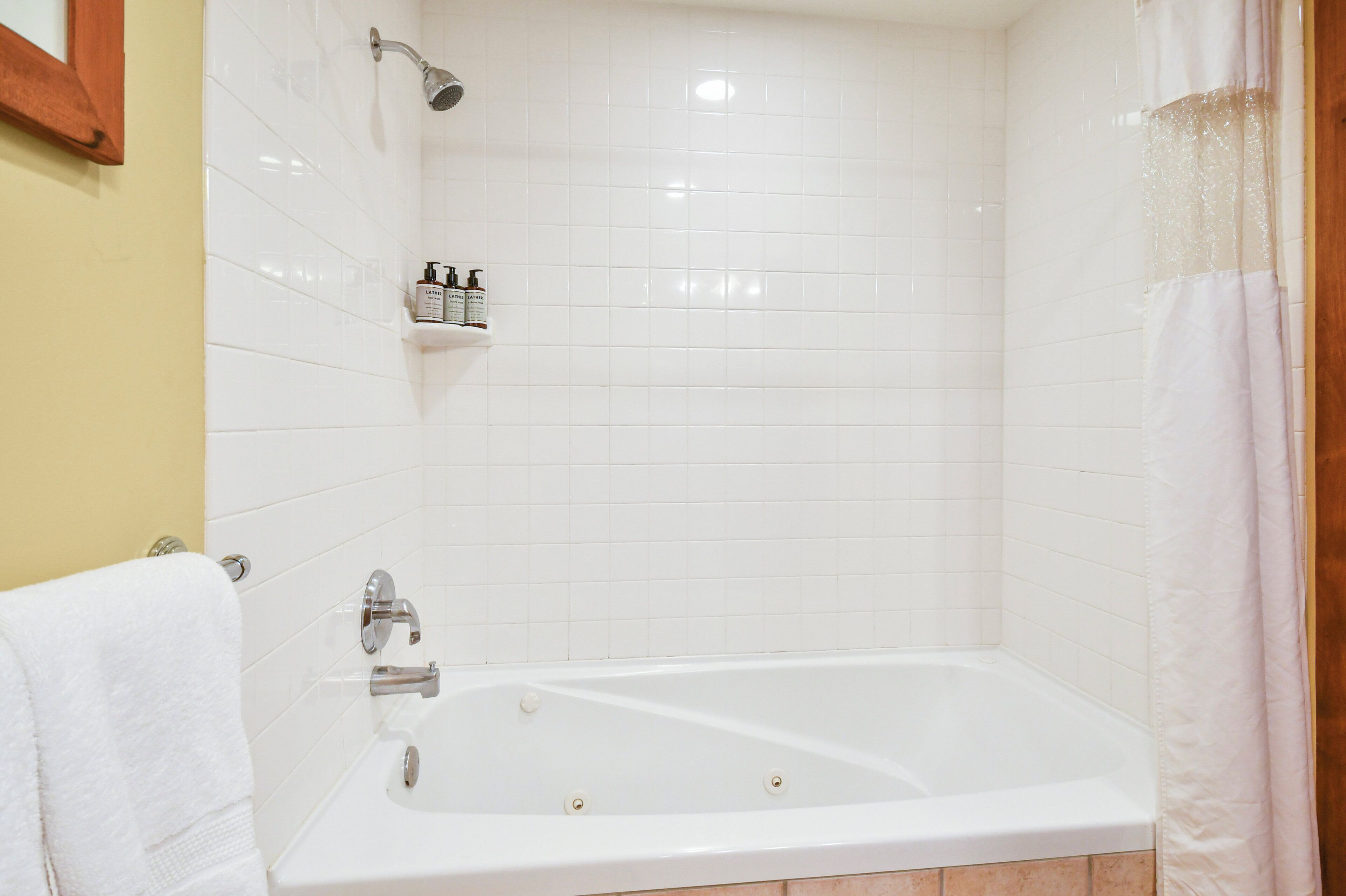 Un bagno con una vasca da bagno bianca, una doccetta e uno scaffale con articoli da toilette.