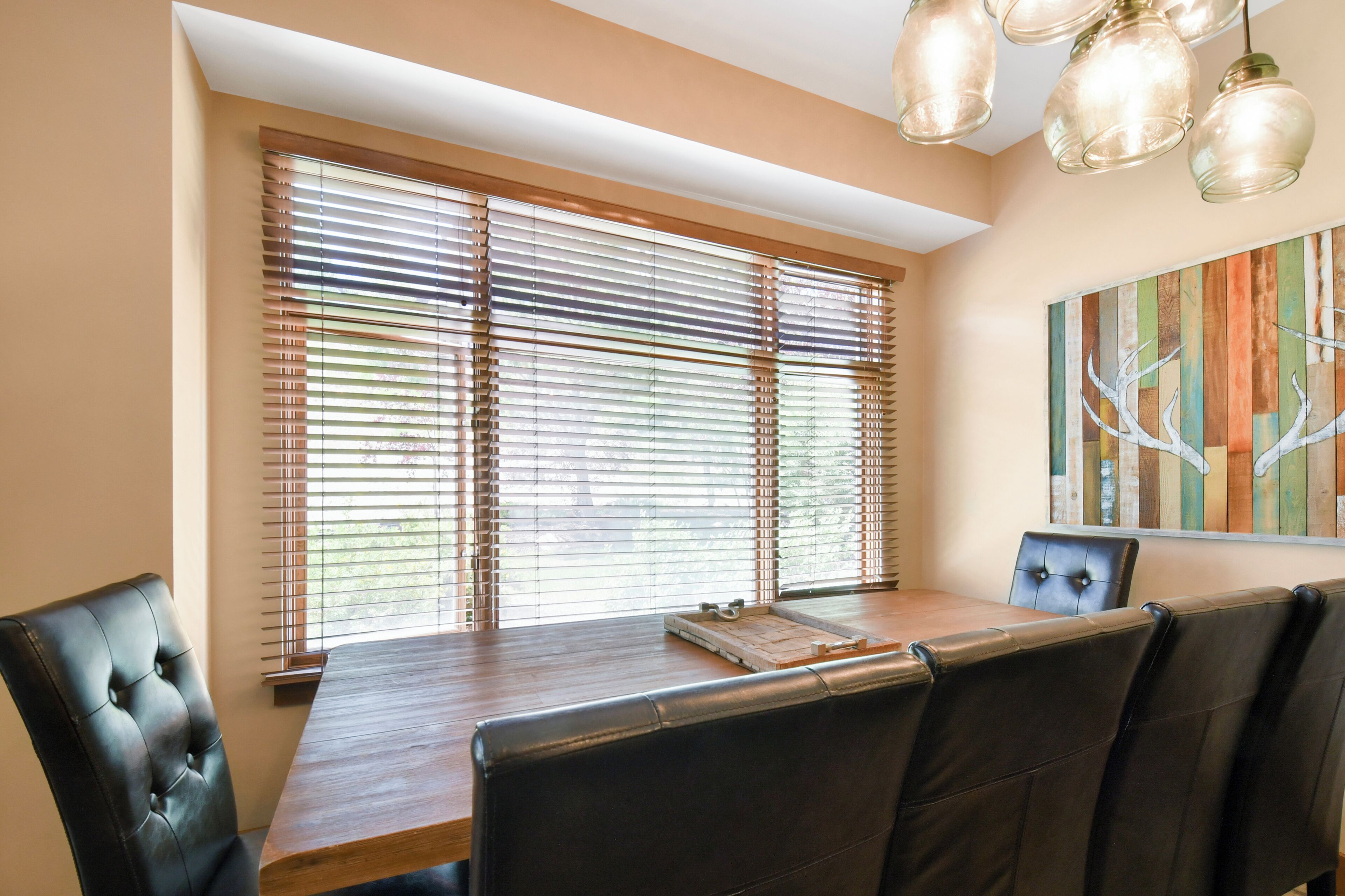 A dining area with a wooden table, black leather chairs, and a window with blinds.