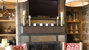 A cozy living room with a fireplace, red patterned sofas, and a glass coffee table.