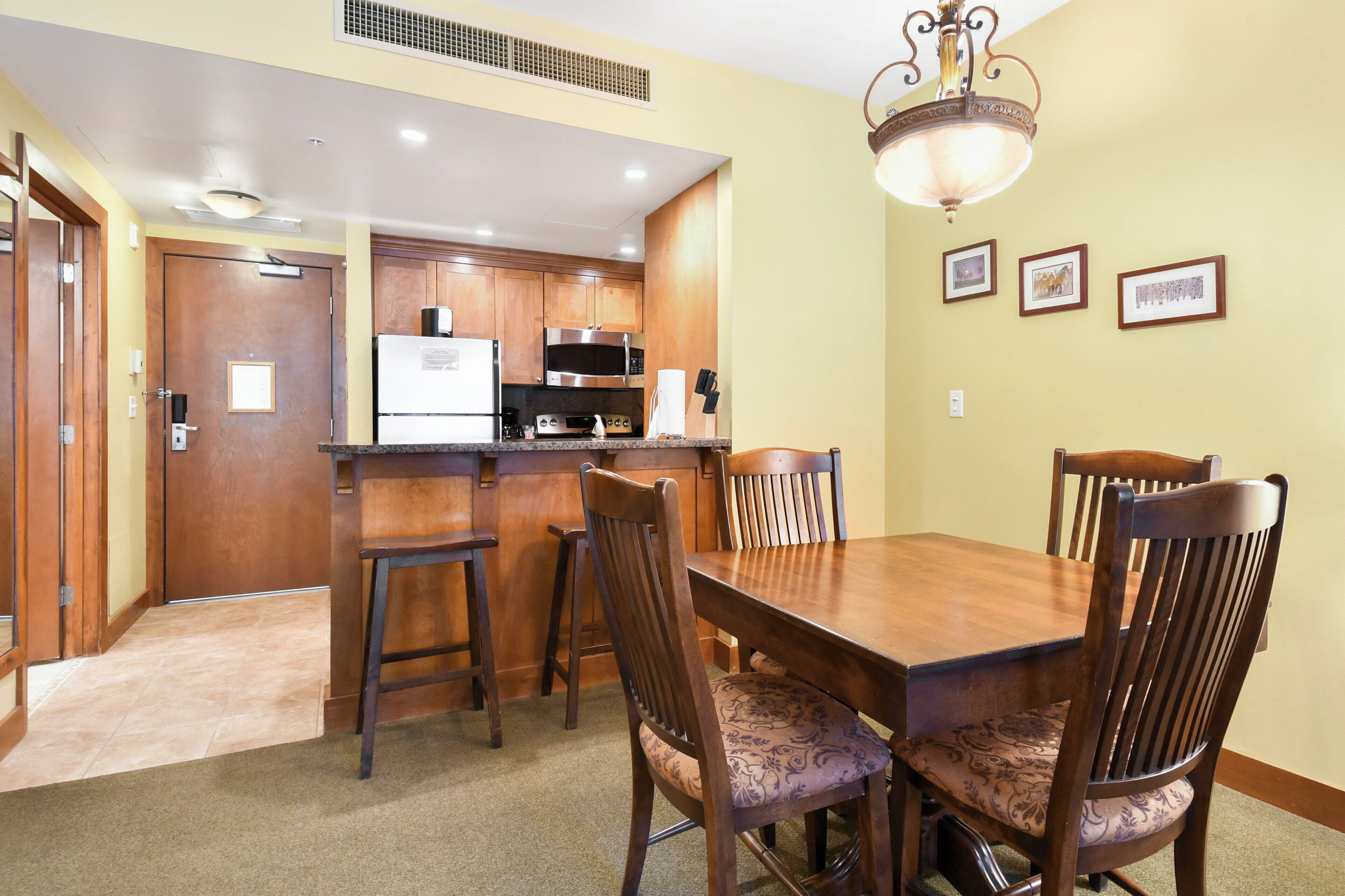 Un comedor con una mesa y sillas de madera, una cocina al fondo y cuadros en la pared.