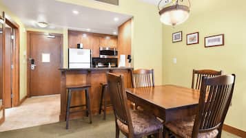 Un comedor con una mesa y sillas de madera, una cocina al fondo y cuadros en la pared.