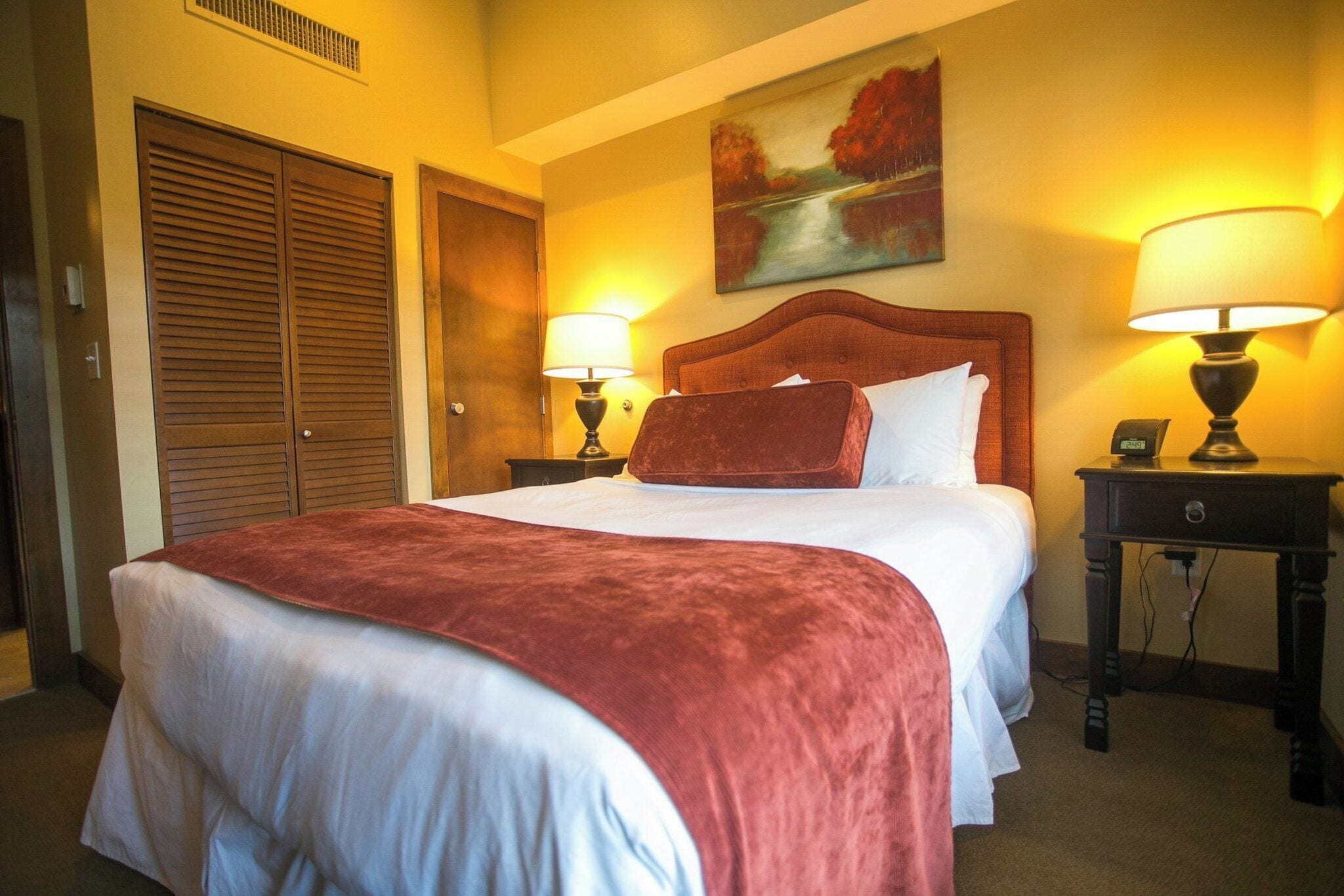 A hotel room with a large bed, two bedside lamps, a painting on the wall, and a wooden door.