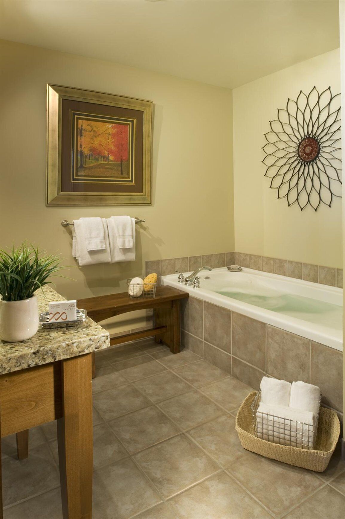 A bathroom with a bathtub, a sink, a mirror, a framed painting, and a decorative wall piece.