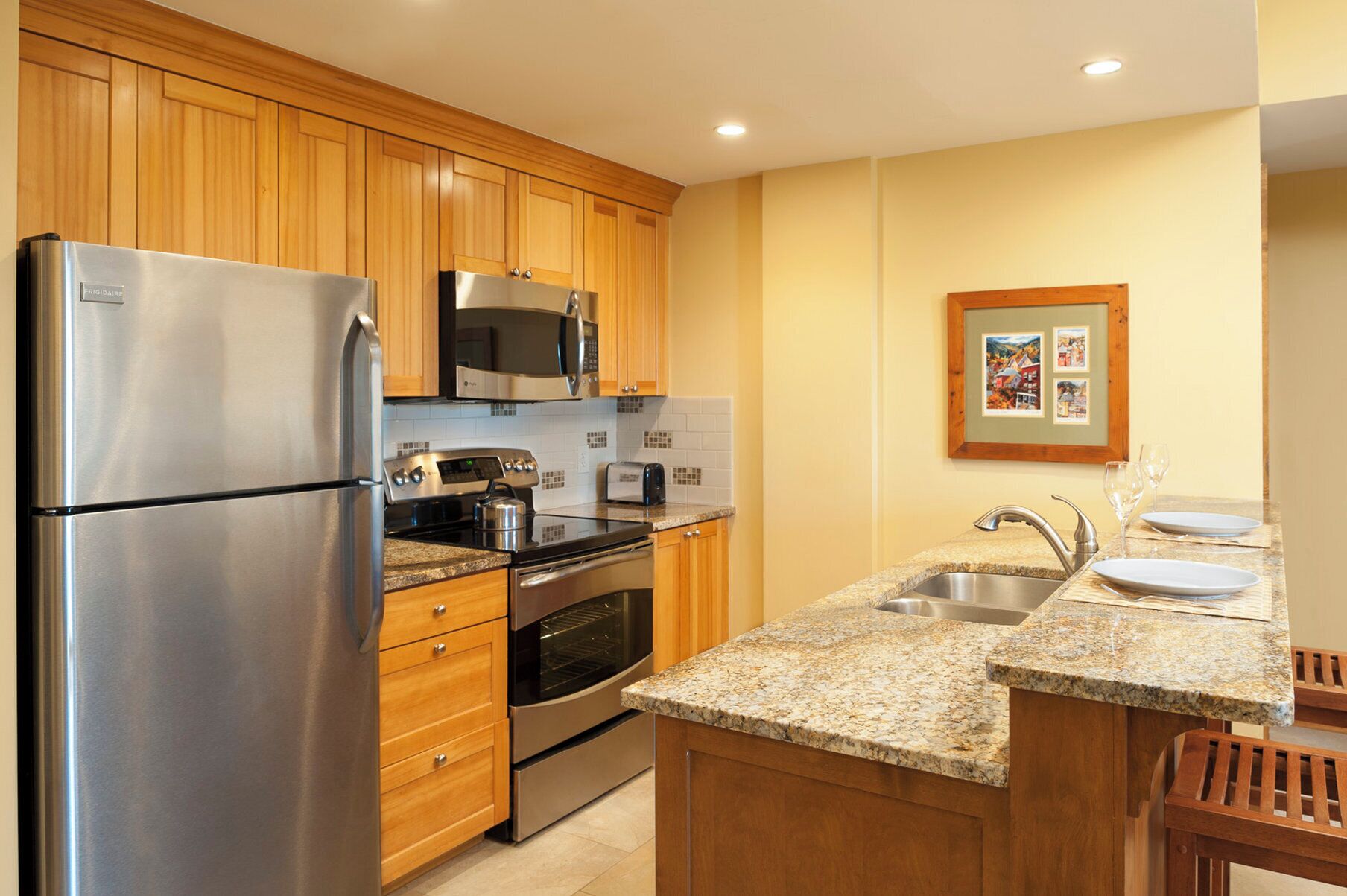 A modern kitchen with wooden cabinets, stainless steel appliances, granite countertops, and a small dining area with a sink and chairs.