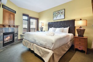 A hotel bedroom with a large bed, a fireplace, and a nightstand with lamps.