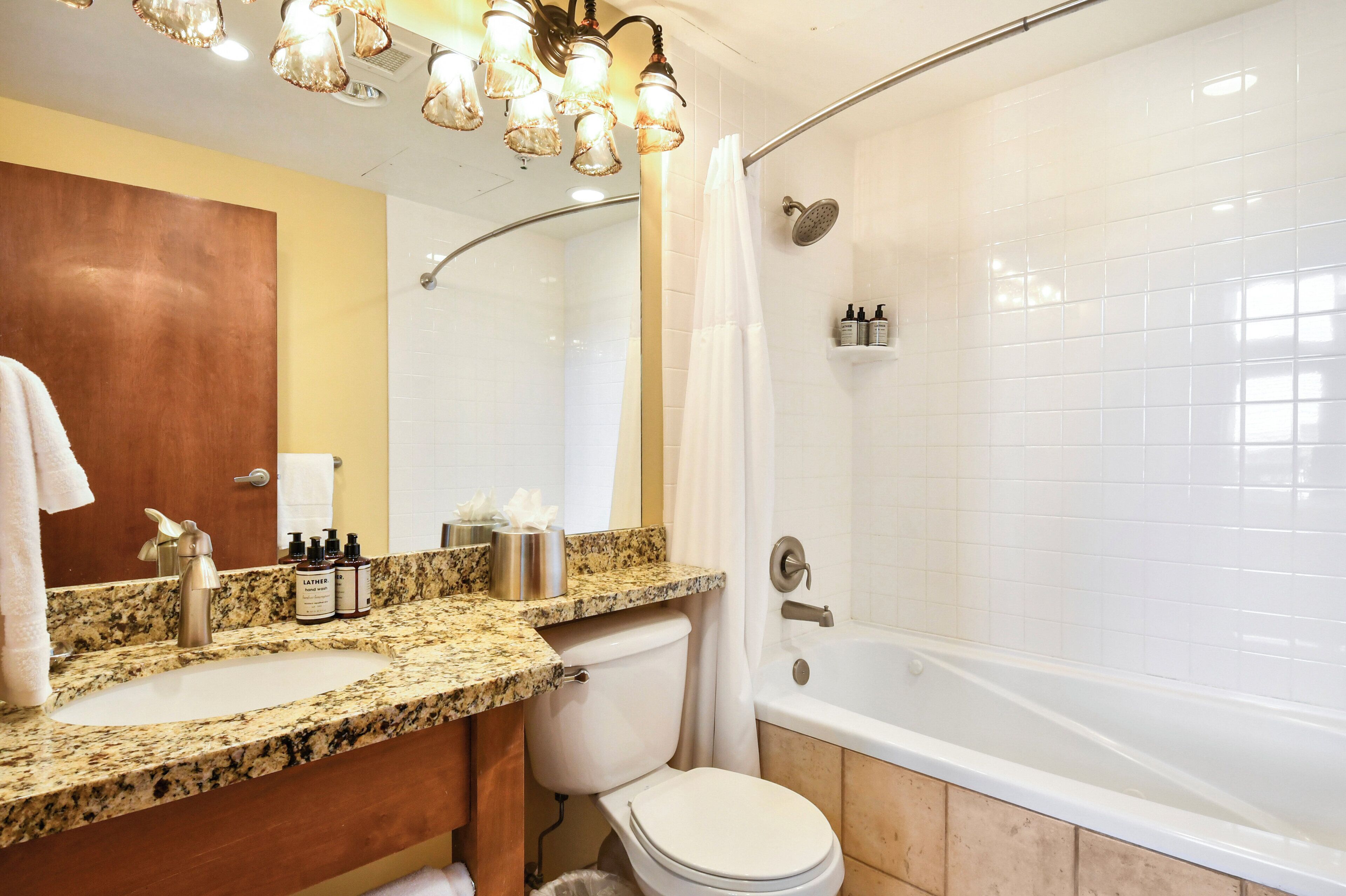Une salle de bain avec un lavabo, des toilettes et une baignoire. On y trouve des articles de toilette sur le comptoir et un rideau de douche.